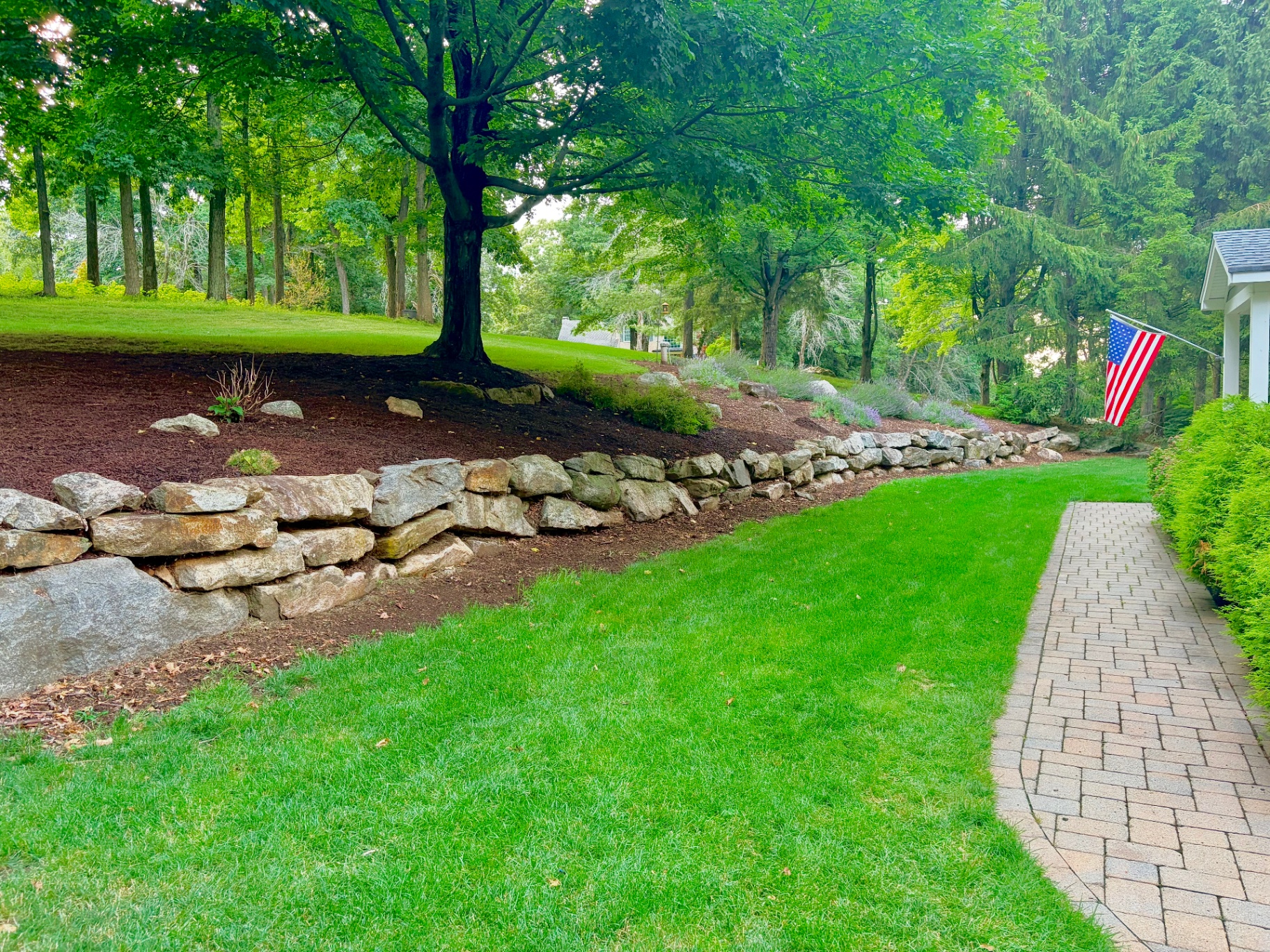 Freshly mulched and edged landscape bed with a stone retaining wall in Morris County, NJ